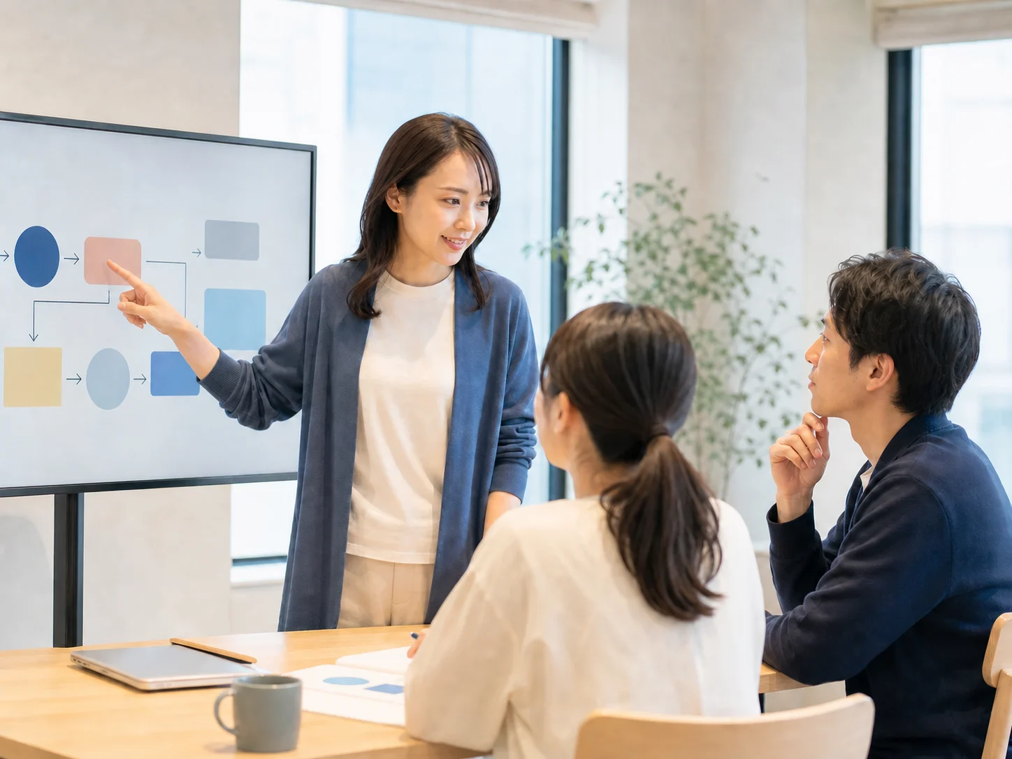 明るいオフィスで業務フローを説明し、参加者と対話する若い日本人女性